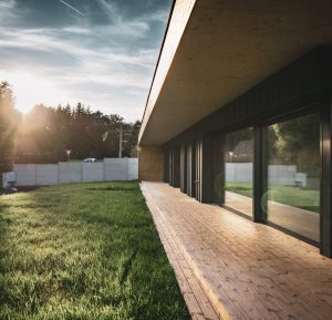 Dřevěná terasa moderní dřevostavby Housenka se zapadajícím sluncem v pozadí